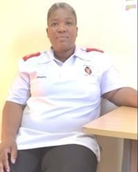 Sr. Phumzile Mbatha sitzt in weißer Pflegeuniform an einem Tisch.