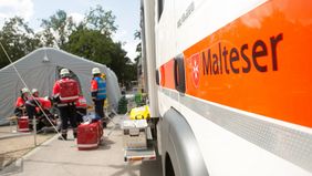 Einsatzkräfte stehen mit Notfallrücksäcken vor einem aufgebauten Zelt.