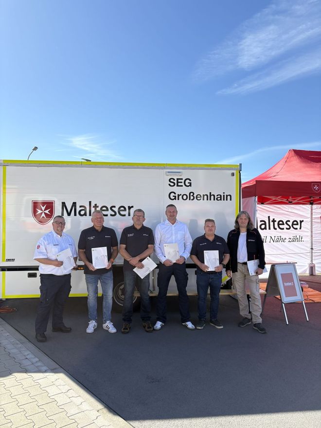 Sechs Malteser stehen mit Urkunden in der Hand vor einem großen Einsatzfahrzeug.
