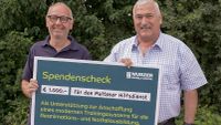 Tobias Cako und Edwin Lambert halten gemeinsam einen symbolischen Spendenscheck.