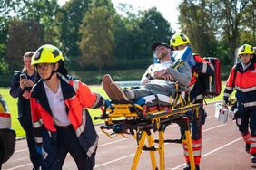 Zwei Malteser fahren einen Verletzen auf einer Trage zum Rettungswagen. 