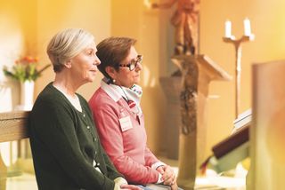 Junge Frau mit Malteser Halstuch ist mit einer älteren Person in einer Kirche