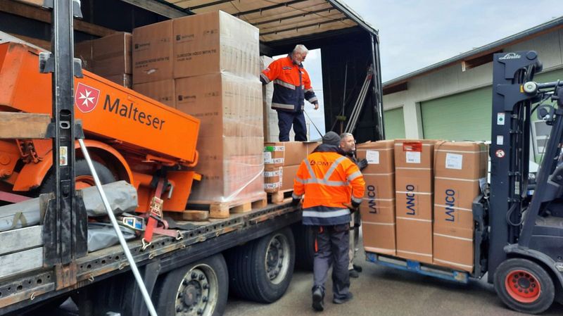 Drei Männer entladen Paletten mit Kartons von einem Lkw.