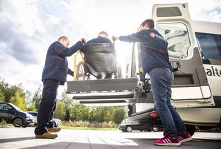 Zwei Mitarbeiter der Malteser befördern einen Rollstuhlfahrer zuverlässig.