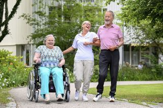 Rollstuhlfahrerin mit einer Pflegerin und einem weiteren Bewohner beim spazieren