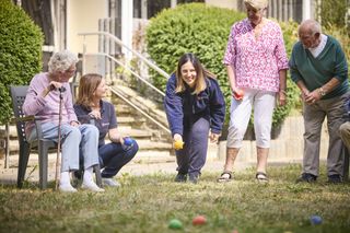 Damen in Malteser Kleidung spielen auf einer Wiese mit Senioren ein Ballspiel