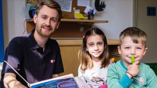 Ein Mann im Malteser Shirt liest zwei Kindern aus einem Buch vor. 