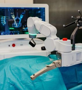 OP-Roboterarm steht über einem abgedeckten Operationstisch, im Hintergrund ist ein Monitor zu sehen.