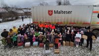 Viele Menschen stehen mit Paketen und vier Malteser Helfern vor dem Glücksbringer-LKW