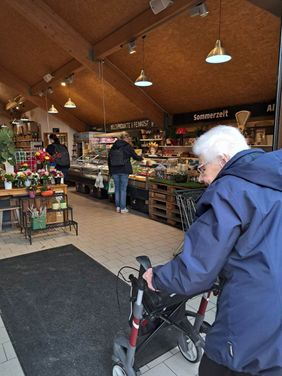 Eine Dame mit Rollator betritt den Eingangsbereich im Hof Löbke, im Hintergrund sind Verkaufsflächen für die dortigen Produkte zu sehen