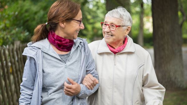 Eine ältere Frau unterstützt eine Seniorin beim Spaziergang