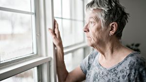 Eine ältere Frau schaut traurig aus dem Fenster.
