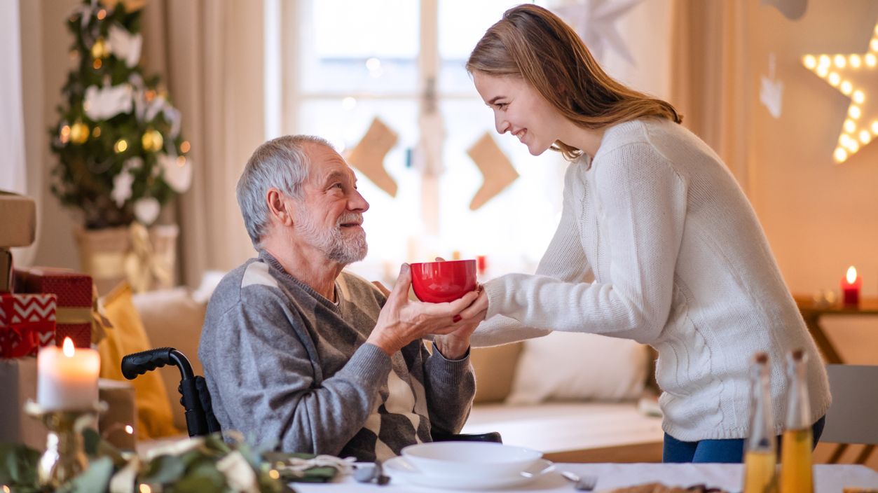 Eine junge Frau gibt einem älteren Mann im Rollstuhl einen Tasse Tee.