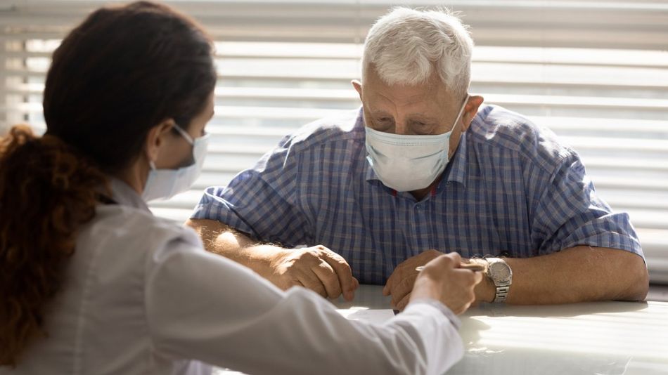 Ein älterer Mann mit Maske wird von einer Ärztin beraten.