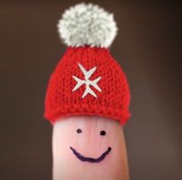 Ein Finger, auf den ein lachendes Gesicht gemalt ist, trägt eine rote Mütze