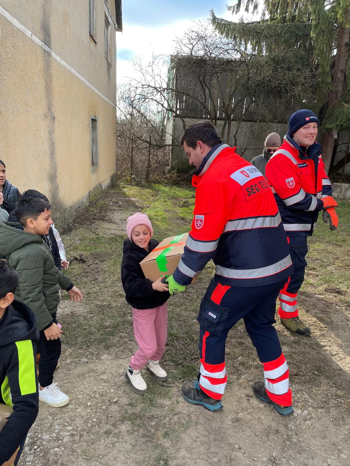 Mann in Malteser Kleidung und Kind mit Weihnachtspaket im Freien