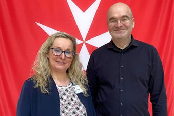 Eine Frau und ein Mann stehen vor einer roten Flagge.