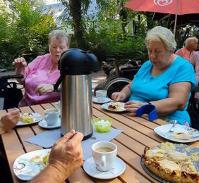 Zwei Frauen sitzen an einem Tisch im Freien, trinken Kaffee und essen Kuchen.