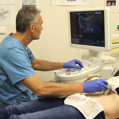 Arzt führt mit Ultraschallgerät eine Untersuchung am Bein eines Patienten durch und blickt auf den Monitor.