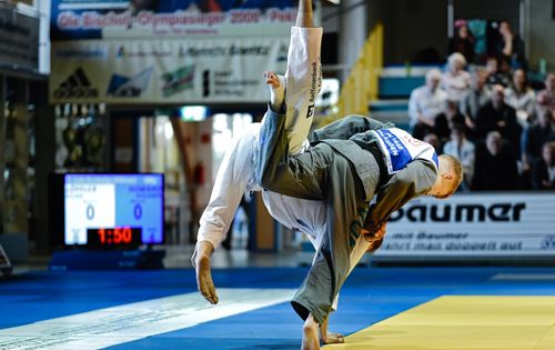 Während eines Wettkampfs wirft ein Judoka den anderen mit einem klassischen Hüftwurf auf der Matte vor Publikum.