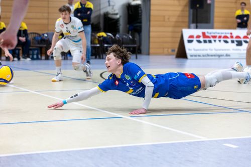 Spieler des SV Schwaig in blauer Kleidung hechtet im Spiel nach dem Ball, Mitspieler und Zuschauer im Hintergrund sichtbar.