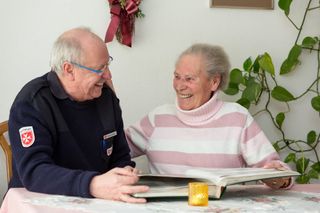 Malteser Mitarbeiter schaut mit einer älteren Dame ein Buch durch