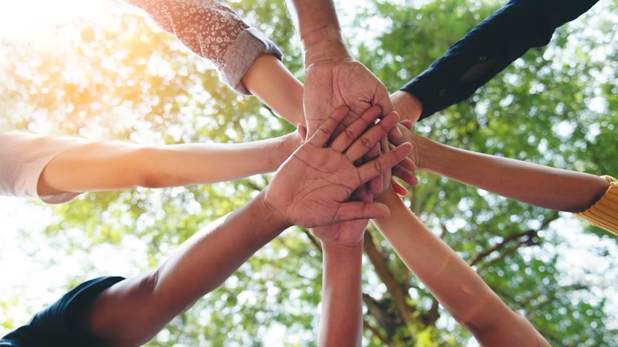 Zusammengelegte Hände mehrerer Menschen von unten fotografiert.