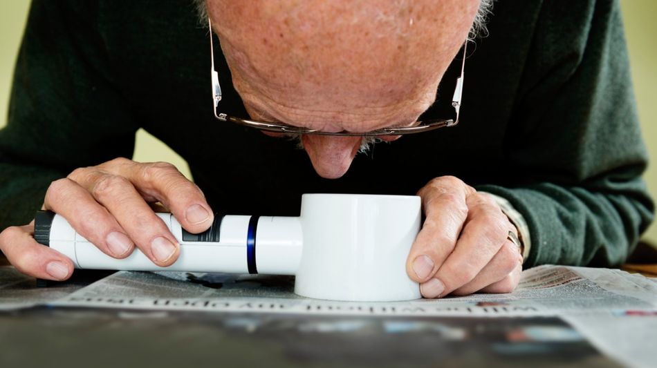 Ein alter Mann liest eine Zeitung mithilfe einer Handlupe mit Beleuchtung.