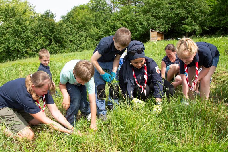 Nour sitzt mit Kindern auf einer grünen Wiese und entfernt Unkraut.