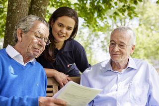 Zwei ältere Männer und eine junge Frau sprechen über ein Dokument, dass einer der Männer in den Händen hält