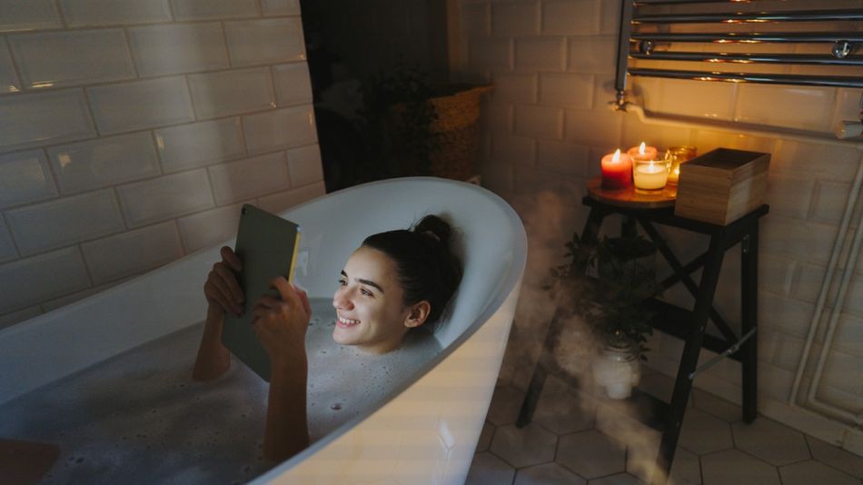 Eine lächelnde Frau mit Tablet in der Badewanne.