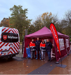 Ehrenamtliche aus der Gliederung Oberhausen stehen unter einem kleinen Pavillon, daneben sieht mal ein Malteser Fahrzeug 
