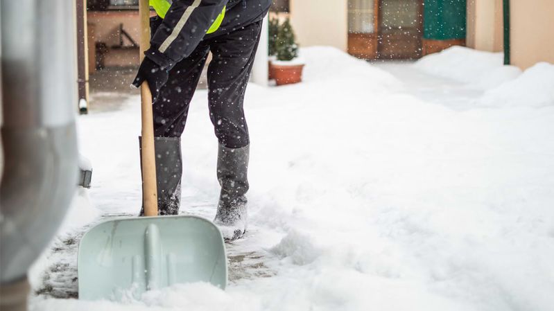 Eine Person in Winterkleidung und Warnweste schippt Schnee.