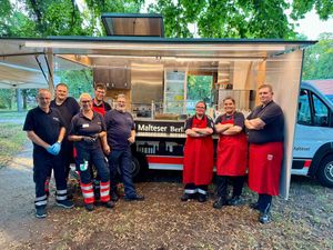 Das Foto zeigt den Gerätewagen Verpflegung mit acht Malteser Helfenden davor.