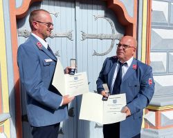 Zwei Männer halten Urkunden und Medaillen.