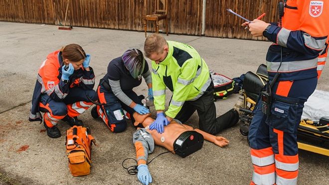 Drei jungen Menschen trainieren unter Beobachtung an einer Übungspuppe die Reanimation