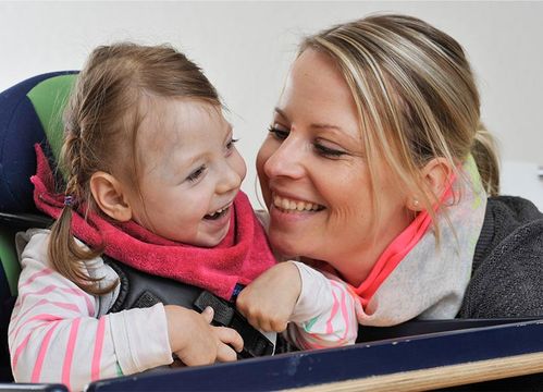 Eine lachende Frau schaut zu einem lachenden Kind, welches in einem Sitzt sitzt