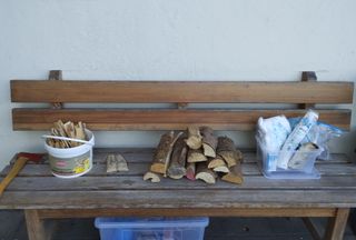Auf einer Holzbank liegen Holzscheite und Utensilien zum Feuermachen
