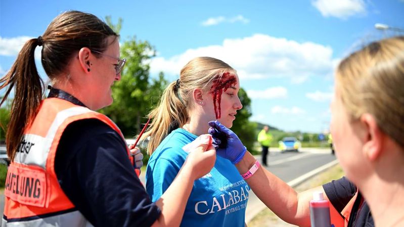 Drei Frauen schminken einem Mädchen eine täuschend echte Wunde ins Gesicht.