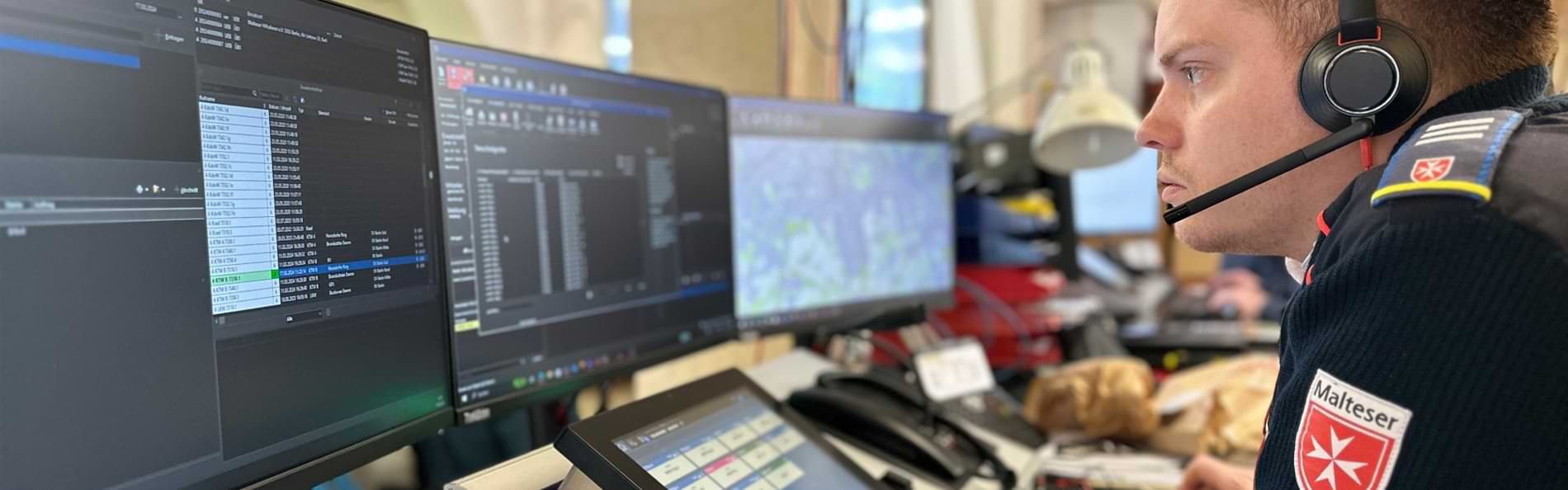 Ein junger Mann mit einem Headset vor Bildschirmen