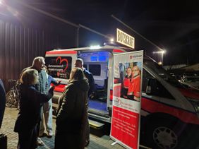 Interessierte informieren sich neben einem Roll-Up und vor dem neuen Herzenswunsch-Krankenwagen über den Dienst