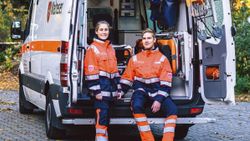 Eine junde Frau und ein junger mann stehen in Einsatzkleidung vor einem Einsatzwagen.