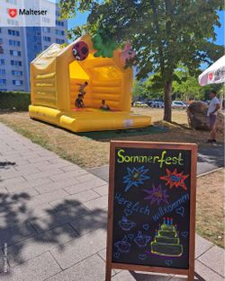 Ein Hinweisschild zum Sommerfest steht vor einer gelben Hüpfburg.