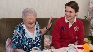 Seniorin lacht herzhaft auf dem Sofa.