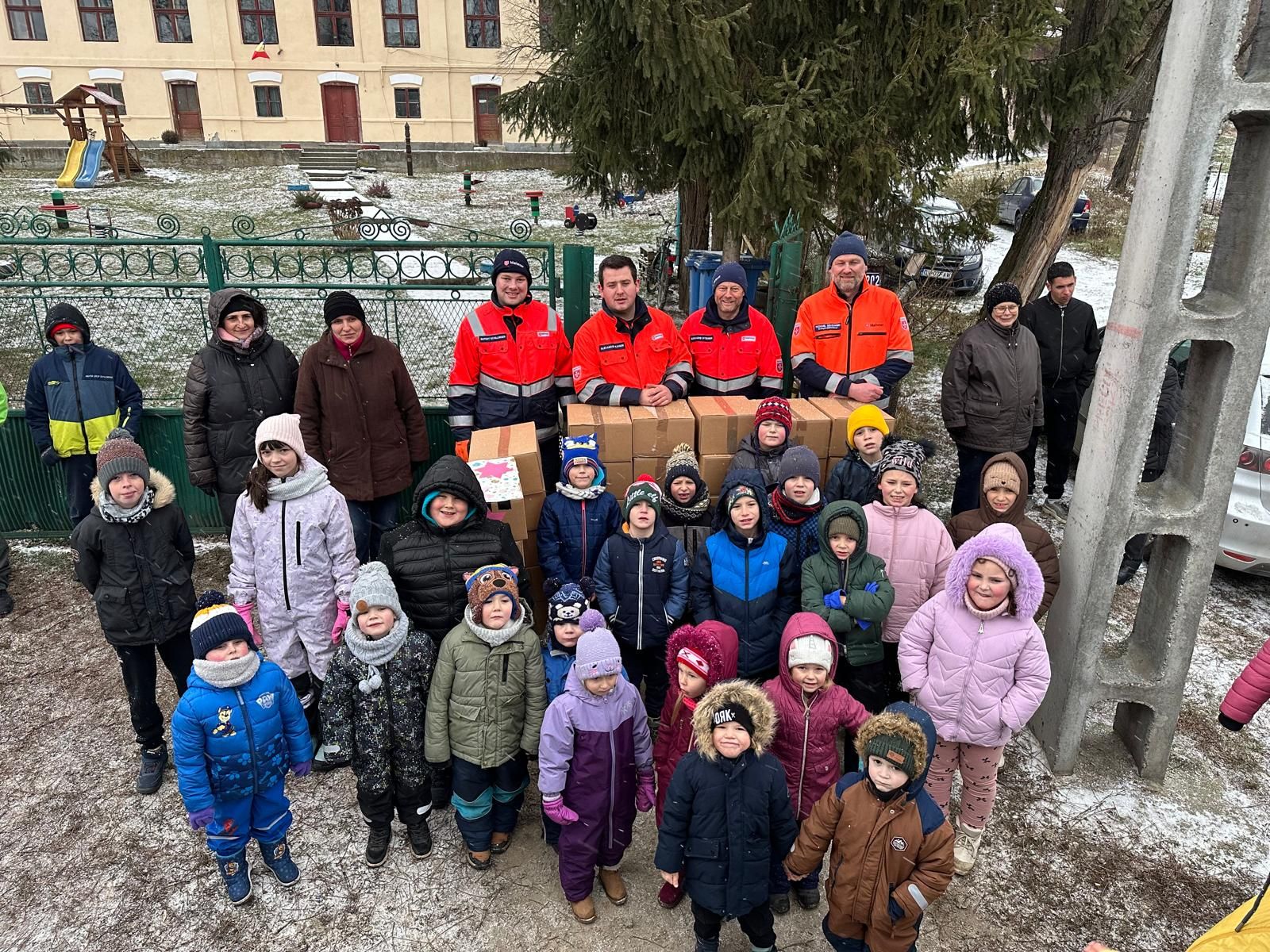 Kinder mit Paketen und Erwachsene stehen vor einem großen gelben Haus