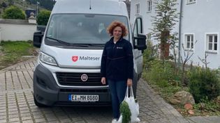 Mitarbeiterin der Malteser steht mit Einkaufstasche vor dem Malteser Einkaufsbus