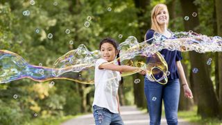 Junge macht große Seifenblasen und wird von Malteser Helferin begleitet.