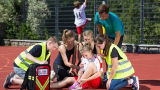 Malteser Schulsanitäter versorgen ein Mädchen, das sich beim Sport verletzt hat.