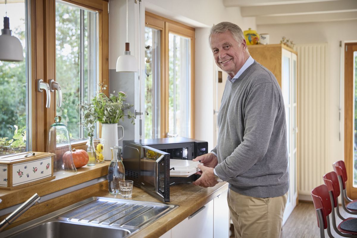 Ein Mann bereitet seinen Menüservice Wochenkarton in der Mikrowelle vor.