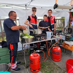 Ein Mann und drei junge Leute stehen an einer mobilen Feldküche.